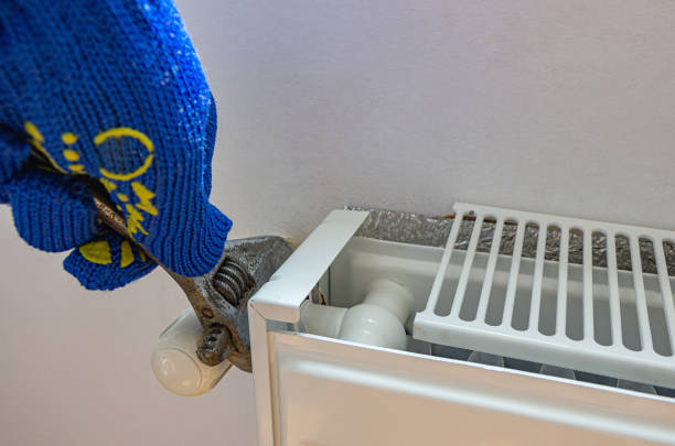 Technician's hand with adjustable wrench repairs a pipe connection to a old heating radiator