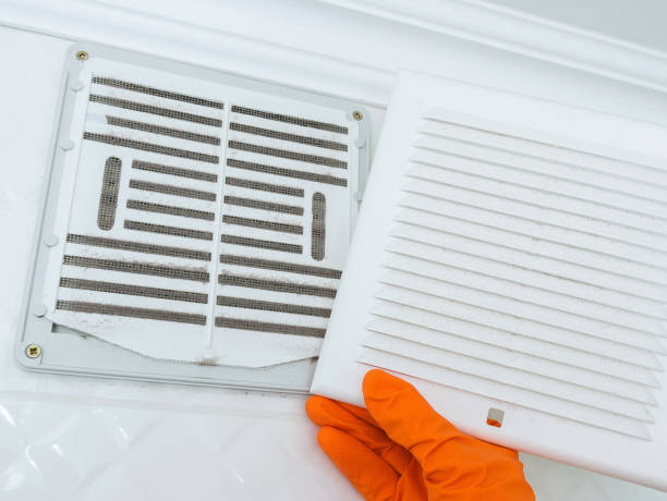 Hand in an protective rubber glove cleans clogged air ventilation grille at home.